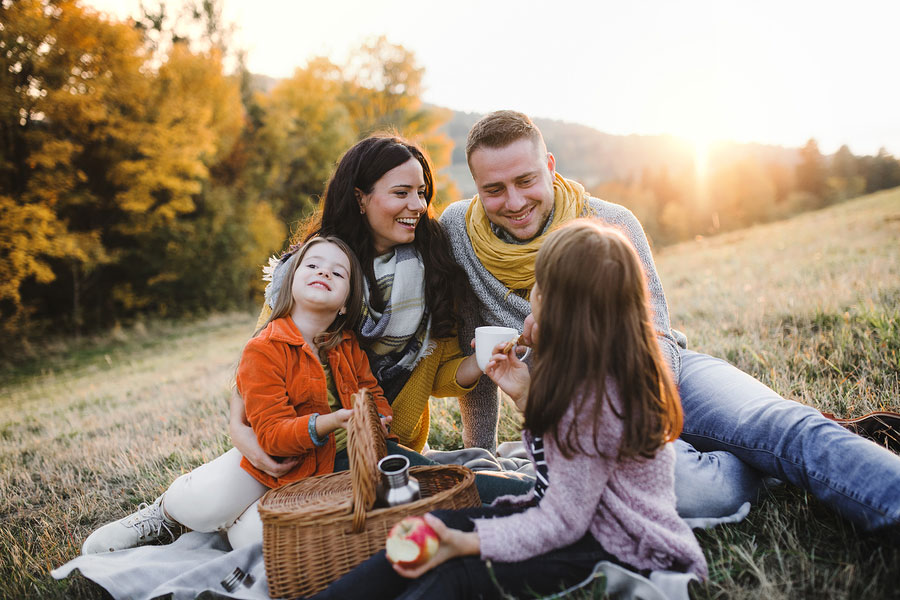 A young family with two small children having picnic in autumn nature at sunset
