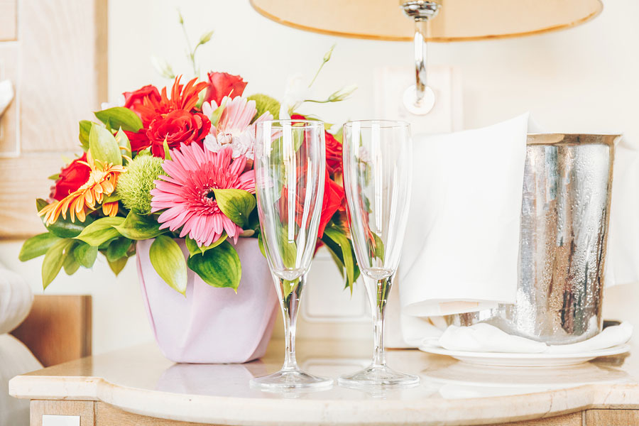 two wine glasses next to a bouquet of flowers in a hotel room